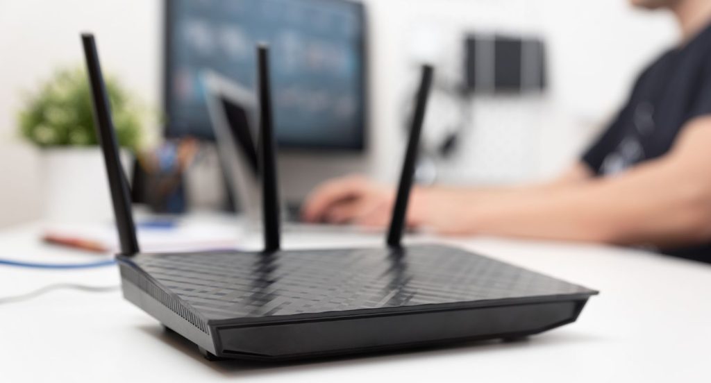 Sort trådløs router med mand og computer i baggrunden
